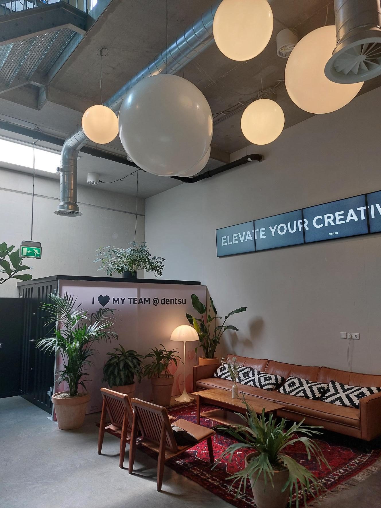 A lounge corner with plants, a leather sofa and large round pendant lights