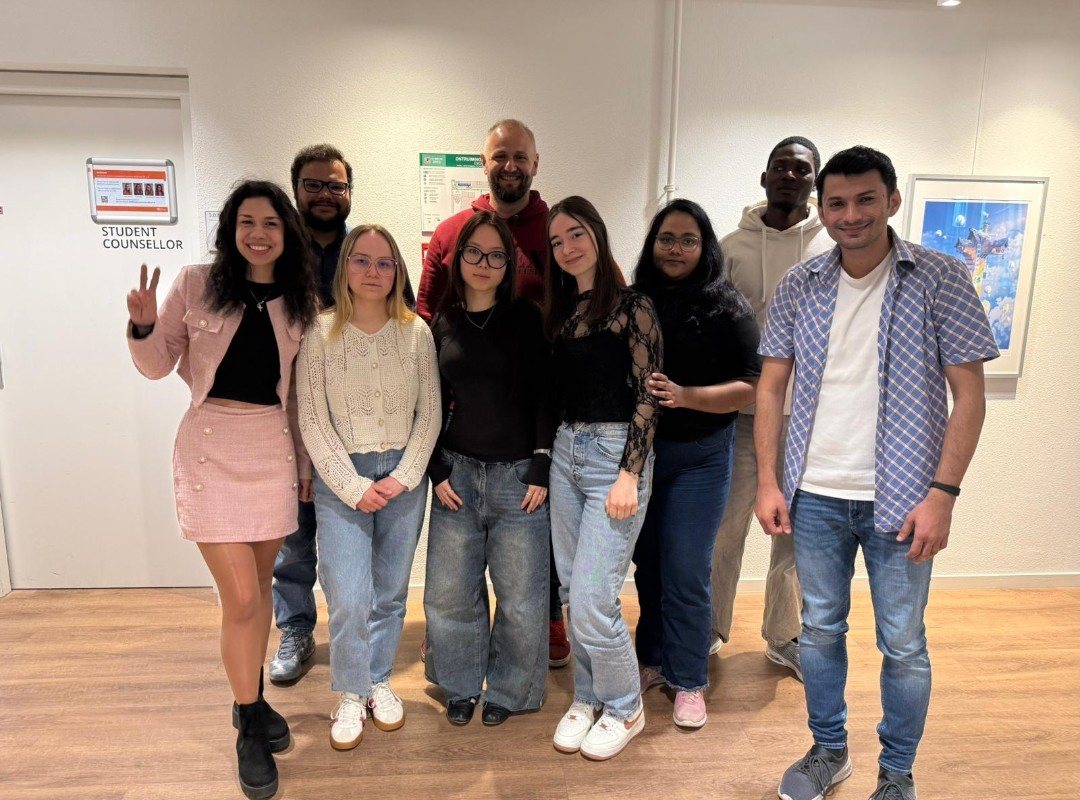 A group of nine people posing together in a corridor