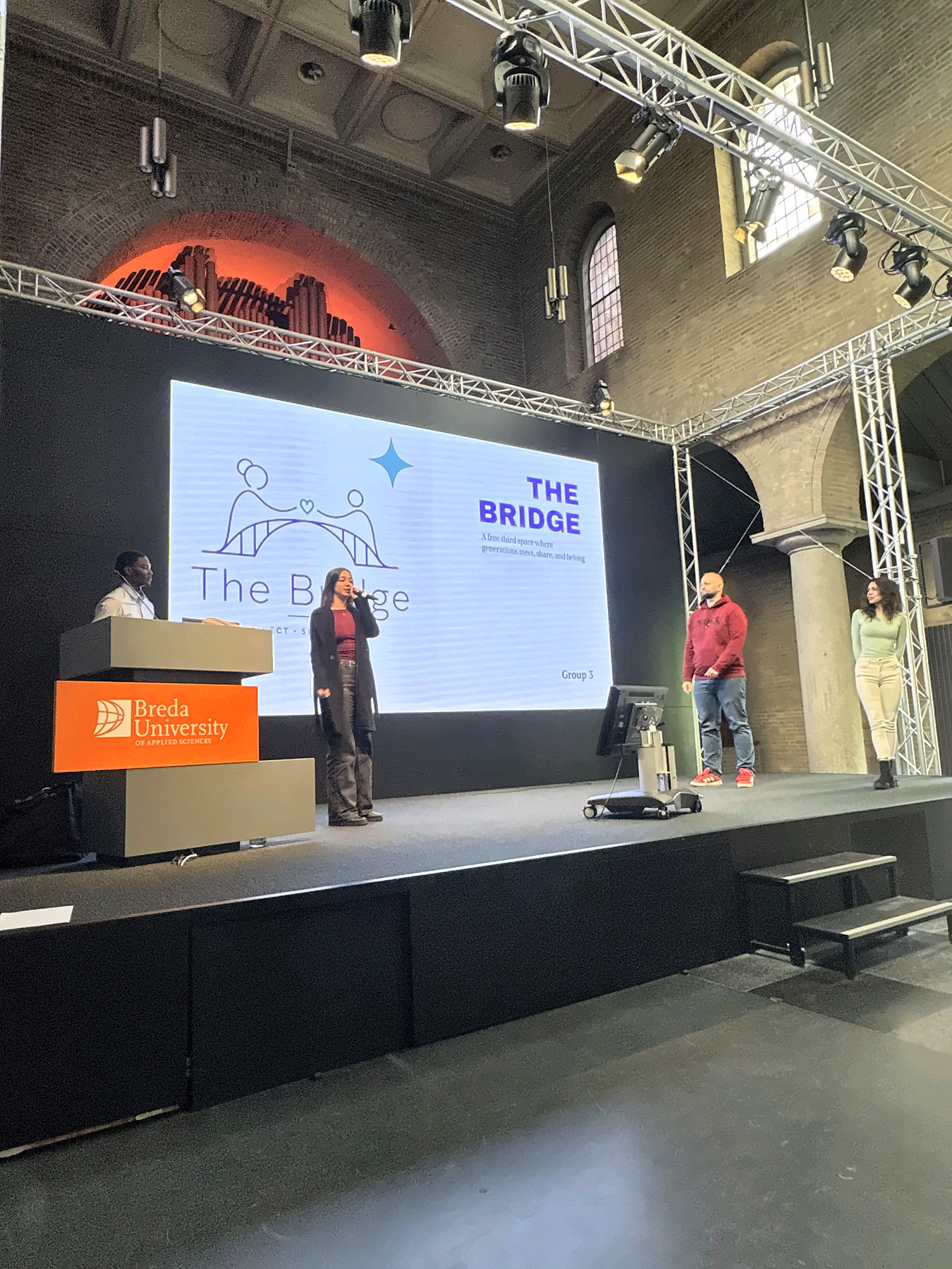 Team members on the Chapel stage in front of the title slide of The Bridge